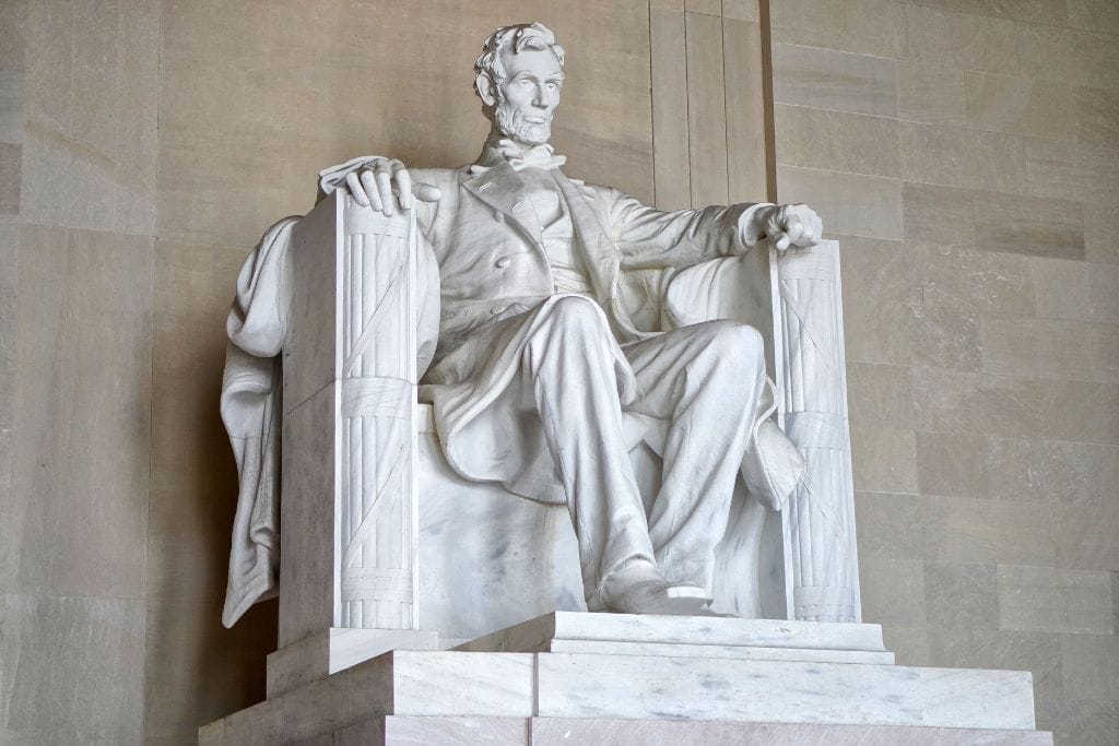 lincoln_memorial This image shows the iconic statue of Abraham Lincoln seated at the Lincoln Memorial in Washington, D.C. The marble statue captures Lincoln in a thoughtful, seated pose with his hands resting on the arms of a large chair, symbolizing strength and leadership amidst the grand, stone interior of the memorial