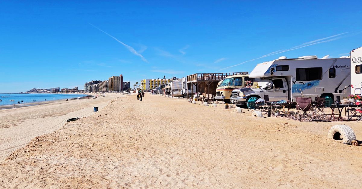 Beachfront RV camping in Rocky Point Mexico with RVs parked along sandy shore near ocean and city skyline in the distance.