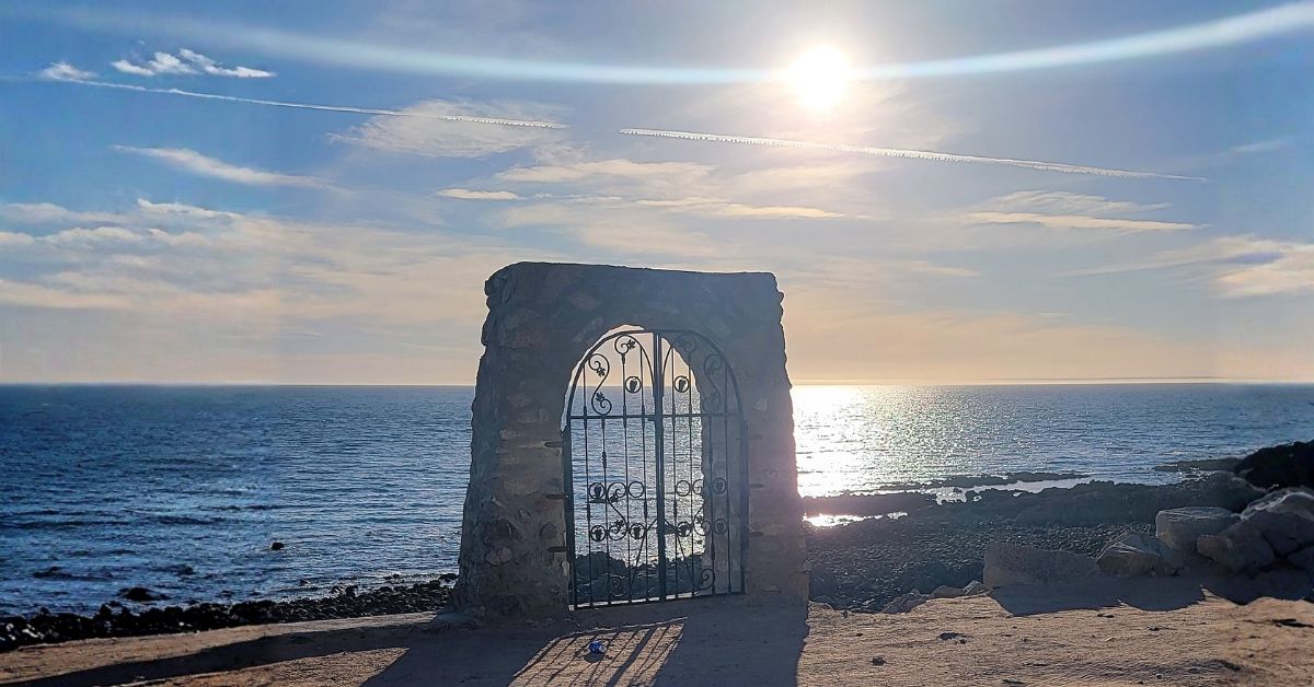 Stone arch gate at Pelican Beach in Rocky Point with sun shining over the ocean and long shadows on the sand
