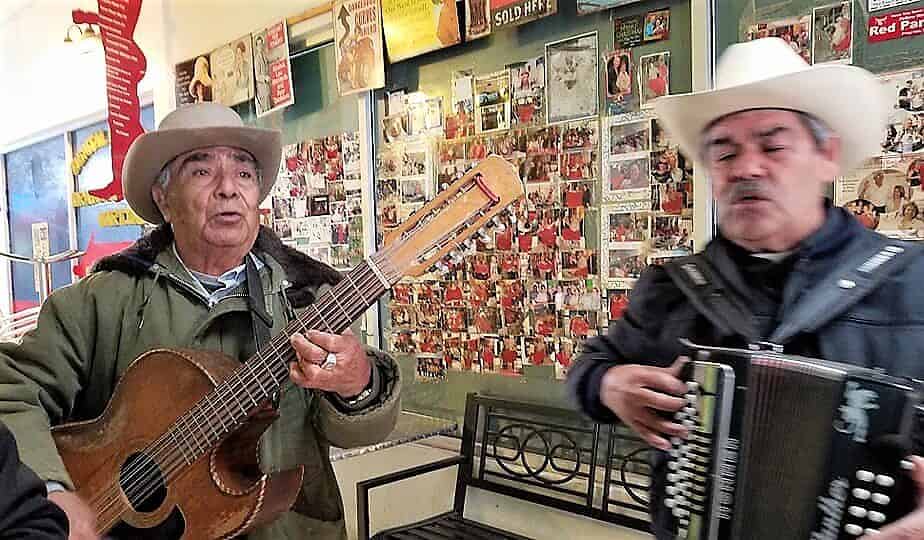 Two mexican men singing and playing guitar and accordion.