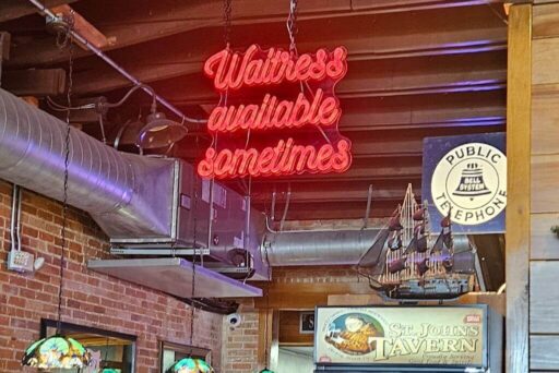 Manatees And More: 25 Things To Do In Crystal River, Florida 2025 34 Interior of a tavern with a humorous neon sign that reads 'waitress available sometimes', next to a vintage public telephone sign and a decorative ship model. The setting has a rustic charm with exposed brick walls and wooden beams.