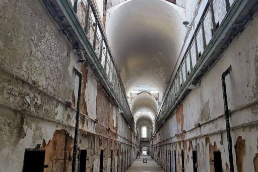 Best Campgrounds Near Philadelphia, Pa For 2025 19 View inside the eastern state penitentiary, showcasing the long, narrow corridor flanked by deteriorating cell walls under a glass roof, with a glimpse of the central guard tower in the distance.