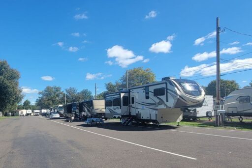 Best Campgrounds Near Philadelphia, Pa For 2025 9 Fifth-wheel trailers and motorhomes lined up in a neat row at a sunny rv park, with trees dotting the background under a clear blue sky with fluffy clouds.