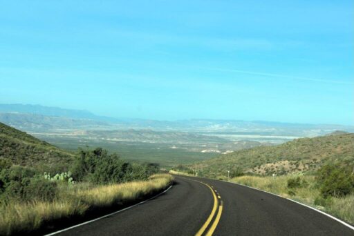 Easy Rv Trip Planning: Preparing For Your Next Adventure 3 A winding road with double yellow lines stretches into a vast landscape of rolling hills and distant mountains under a clear blue sky.