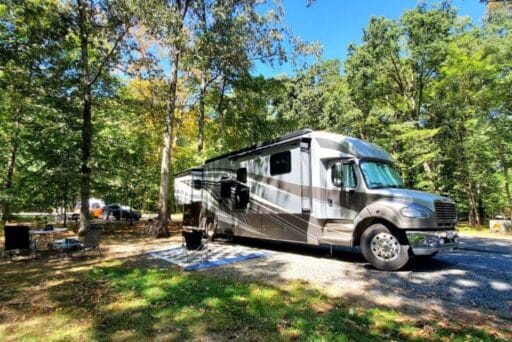 Rv Friendly Campgrounds Near Washington, Dc 2025 9 A large, luxury rv is parked at a spacious campsite in bull run regional park, surrounded by lush green trees under a clear blue sky. Outdoor chairs, a mat, and bicycles are set up nearby, creating a cozy and inviting camping atmosphere amidst the forested setting.
