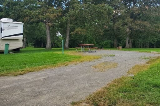 Rv Friendly Campgrounds Near Washington, Dc 2025 6 A campground featuring a parked rv on a gravel pad with a red picnic table and a fire ring nearby. The area is surrounded by grassy open spaces and mature trees, creating a blend of natural shade and open lawn. This spot offers a cozy setup for rv camping with convenient outdoor seating and a fire pit for evening gatherings.