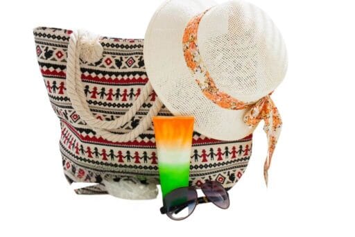 Swim With Manatees In 2025: An Unforgettable Adventure 6 This image shows a summer-themed setup, including a patterned tote bag with a tribal-inspired design, a straw hat with a floral scarf tied around it, a colorful gradient sunscreen bottle, and a pair of sunglasses.
