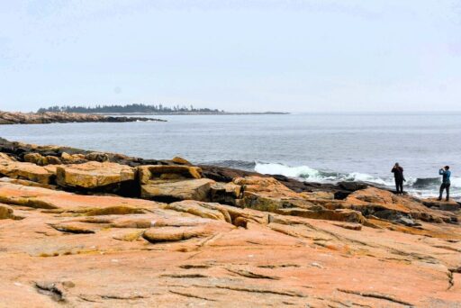 The Ultimate Acadia National Park Itinerary For 2025: Your Perfect 3-Day Plan 18 Schoodic point in acadia, featuring rugged coastal rocks, ocean waves, and two visitors taking photos of the scenic shoreline.