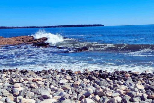 Beaches In Acadia National Park: More Than Just Sand 15 Waves crash against rocky shores at a pebble beach under a bright blue sky at seawall, acadia.