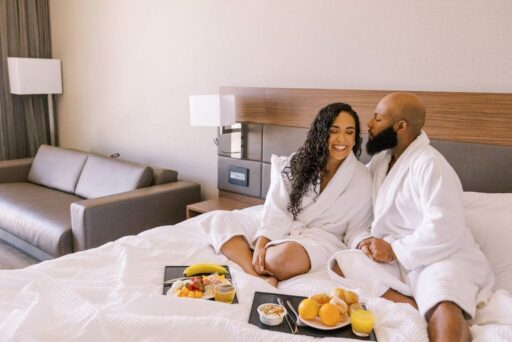 30 Best Things To Do In Batavia, Ny In 2025 23 Couple in white robes enjoy breakfast in bed at a batavia, ny hotel, smiling and relaxing with fruit, juice, and pastries on trays.