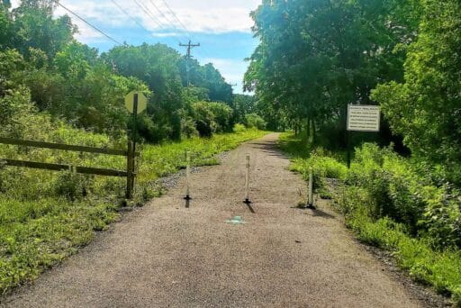 30 Best Things To Do In Batavia, Ny In 2025 11 Sunny entrance to ellicott trail in batavia, ny, with gravel path, trail rules sign, greenery, and utility poles lining the route.