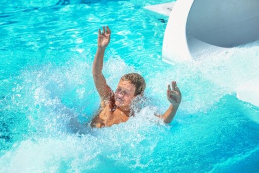 30 Best Things To Do In Batavia, Ny In 2025 22 Child splashes into a bright blue pool from a water slide at palm island indoor waterpark in batavia, ny, arms raised in excitement.