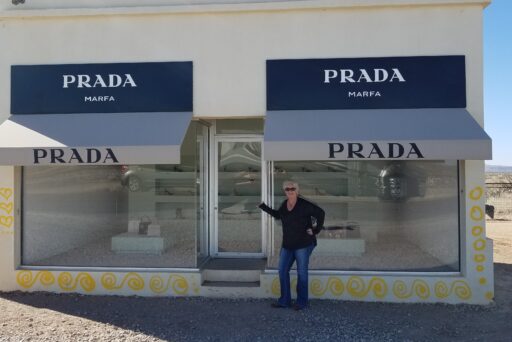11 Fun Things To Do In Terlingua You Can’t Miss In 2025 24 Person poses in front of the prada marfa art installation in the desert, with purses and shoes displayed behind glass.