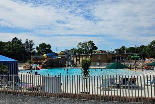 Best Campgrounds Near Philadelphia, Pa For 2025 6 Outdoor pool with waterslides and lounge chairs at a family campground near philadelphia, pa, under a partly cloudy sky.