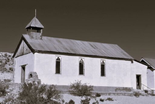 11 Fun Things To Do In Terlingua You Can’t Miss In 2025 6 St. Agnes church in terlingua, texas, with a wooden bell tower and arched windows, captured in a black-and-white desert setting.
