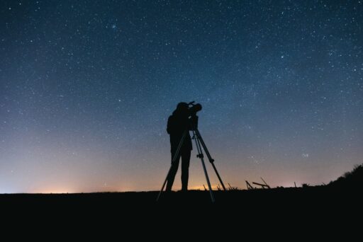 11 Fun Things To Do In Terlingua You Can’t Miss In 2025 14 Silhouette of a person using a telescope under a star-filled night sky with faint horizon glow in the distance.