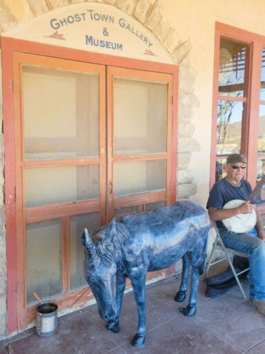 11 Fun Things To Do In Terlingua You Can’t Miss In 2025 7 Man plays banjo on a porch beside a donkey sculpture at the ghost town gallery & museum in terlingua, texas.