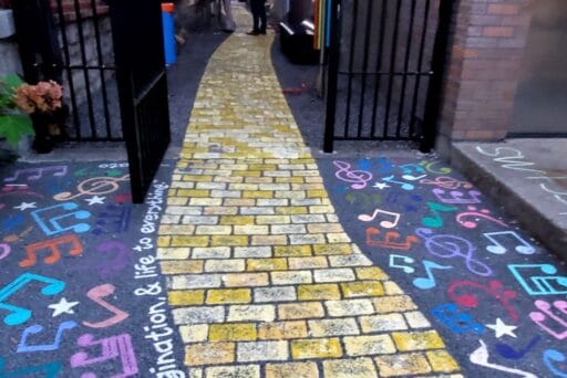 30 Best Things To Do In Batavia, Ny In 2025 25 A yellow brick path winds through a gated alley, bordered by colorful music notes and the phrase