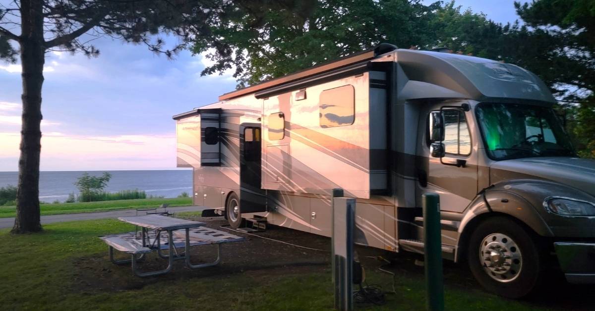 Lakefront RV campsite at sunset – one of the best RV destinations Motorhome at a lakefront campsite during sunset with trees and picnic table, highlighting one of the best RV destinations.