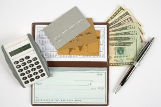 The Complete Guide To Full-Time Rv Living 3 Calculator, credit cards, checkbook, and cash laid out on a white surface with a pen