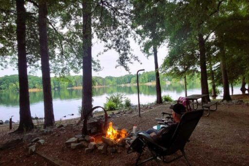 The Complete Guide To Full-Time Rv Living 9 Person relaxing by a lakeside campfire surrounded by trees at a quiet wooded campsite