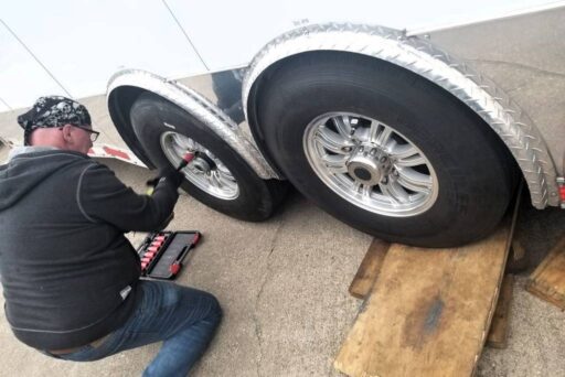 The Complete Guide To Full-Time Rv Living 8 Man using power tool to tighten trailer tire lug nuts while kneeling on pavement
