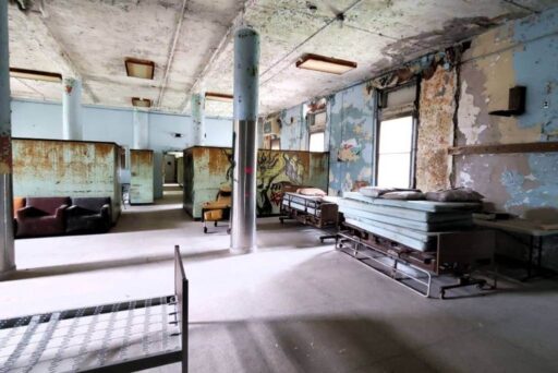 Inside An Abandoned Asylum: A Haunting Roadside Attraction Peeling paint, rusted partitions, and old hospital beds fill a decaying room inside an abandoned asylum turned roadside attraction.