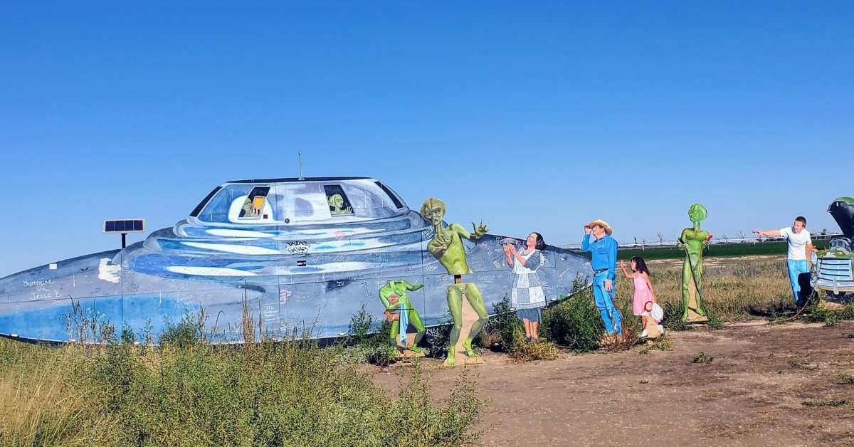 Alien Encounter Roadside Attraction in New Mexico Cartoon-style alien roadside attraction in New Mexico with spaceship crash scene, green truck, and wooden figures pointing at the sky.