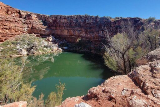 Bottomless Lakes State Park: A Natural Wonder Near Roswell A green, reflective lake sits in a circular sinkhole surrounded by rocky red cliffs and desert vegetation near roswell.
