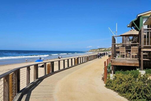 Crystal Cove Boardwalk, A Slice Of Americana Charming wooden boardwalk along the beach with colorful vintage cottages and people strolling in crystal cove state park, california.