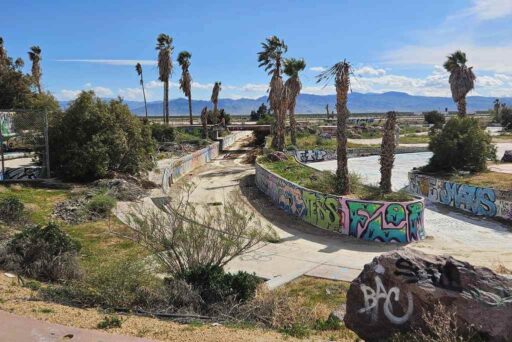Graffiti-covered lazy river and crumbling palm trees at the abandoned lake dolores waterpark in the mojave desert.
