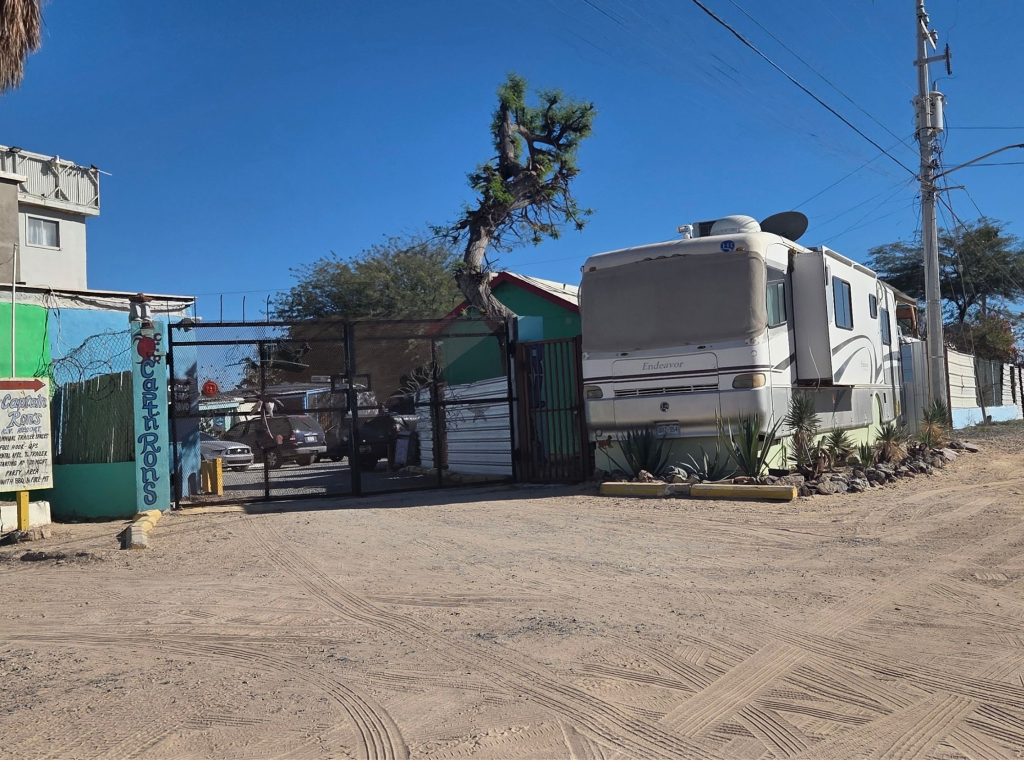 Entrance to captain ron's rv park in rocky point mexico with gated access rv parked outside and sandy road leading through area.