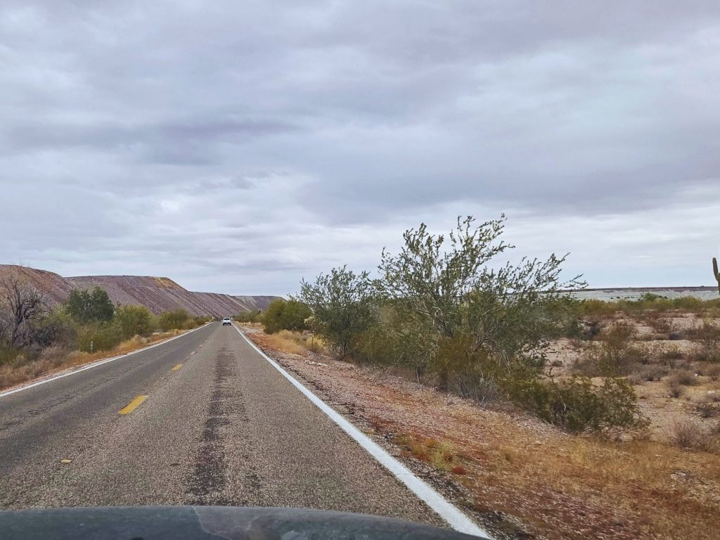 Two lane desert highway leading to rocky point mexico with cactus scattered landscape and overcast sky during road trip.