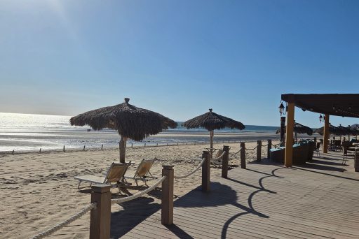 Beach loungers under thatched umbrellas facing the ocean in puerto peñasco with soft morning light reflecting off the water. The quiet and relaxed setting captures the kind of slow beach days that make it easy to stay longer in puerto peñasco.
