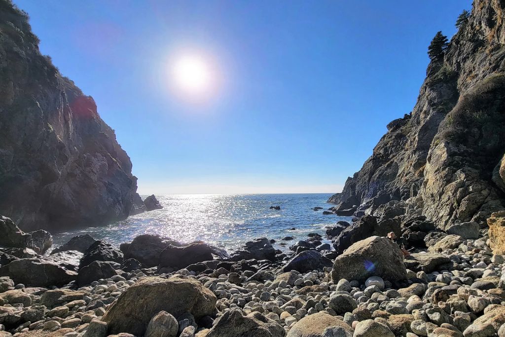 Rocky shoreline at paddington cove in big sur with steep cliffs and sunlit ocean water between the rocks.