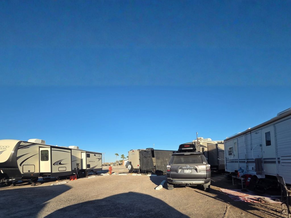 Rvs and trailers parked in gravel sites at playa bonita rv park in rocky point mexico with clear blue sky and open layout.