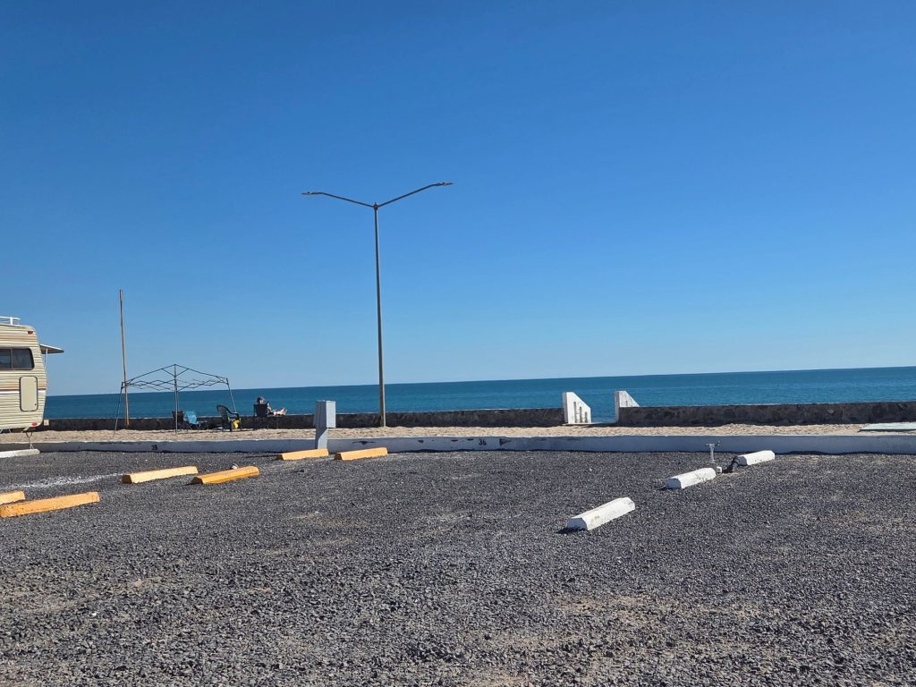 Gravel rv sites at playa de oro in rocky point mexico facing ocean seawall with clear blue sky and open beachfront camping area.