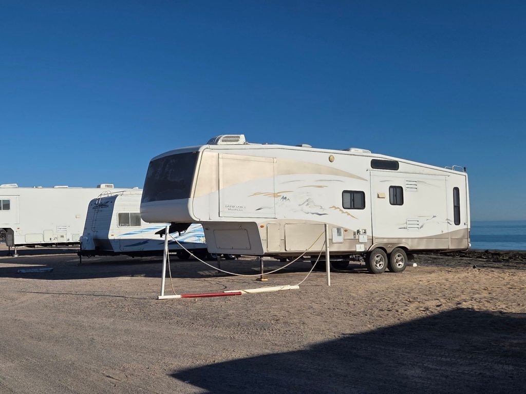 Fifth wheel rv parked at the reef rv park in rocky point mexico beside calm water and rocky breakwater under clear sky