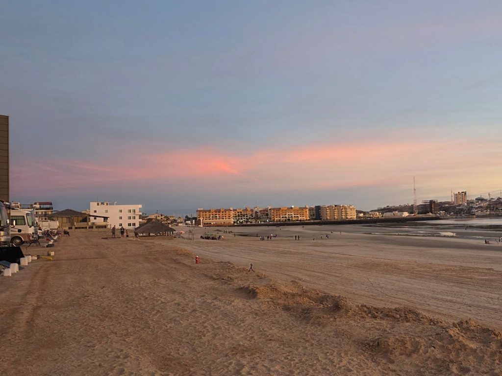 Sunset at rocky point mexico beach with rvs parked along shore people walking and colorful sky over calm ocean.