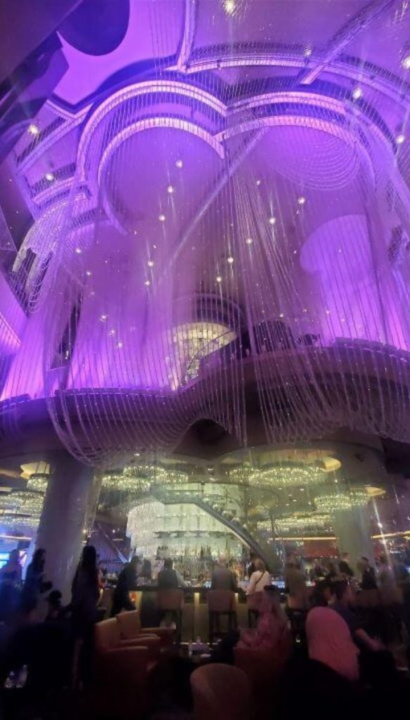 The chandelier bar in las vegas with purple lighting and multi level crystal strands above a busy lounge