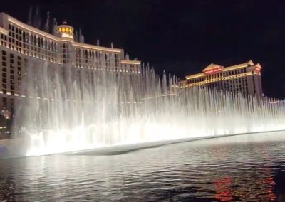 Bellagio fountains at night with water jets in front of illuminated hotels on the central strip. A top area for where to stay in las vegas.