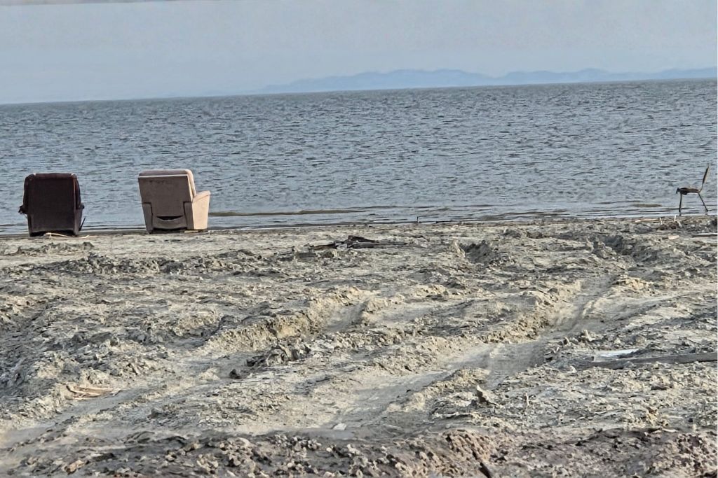 Visiting The Salton Sea: California’s Strangest Desert Lake 3 Two abandoned chairs facing the salton sea on a cracked and barren desert shoreline.