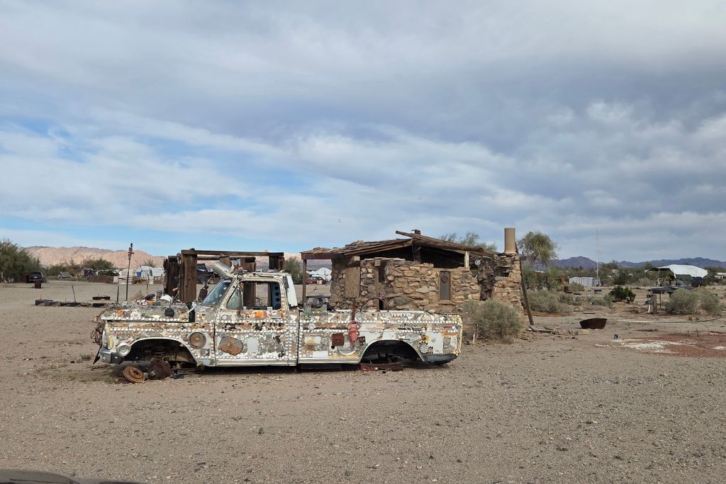 Visiting The Salton Sea: California’s Strangest Desert Lake 6 Abandoned truck and crumbling buildings in slab city beneath dramatic desert storm clouds.