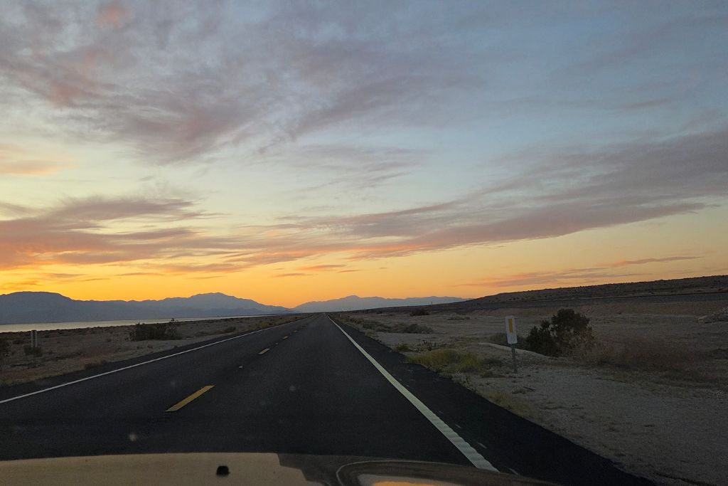 Visiting The Salton Sea: California’s Strangest Desert Lake 16 Empty desert highway near the salton sea at sunset with mountains silhouetted against the sky.