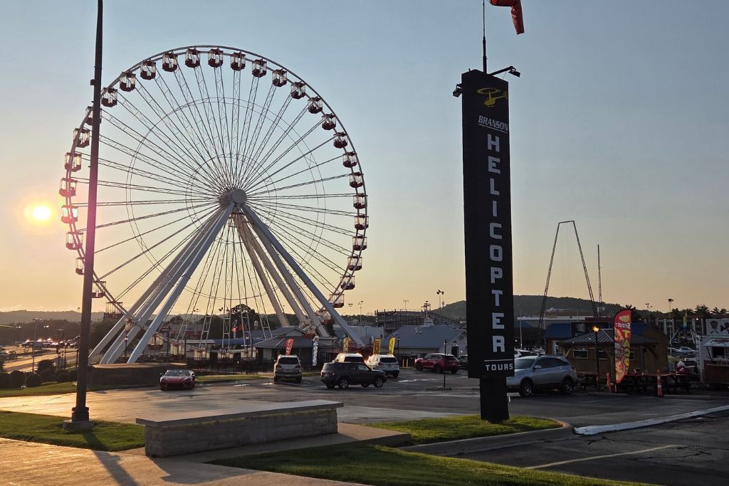 Missouri Road Trip Itinerary: Branson, The Ozarks &Amp; Beyond 19 Branson ferris wheel at sunset beside the branson helicopter tours sign with attractions and restaurants lining the strip.