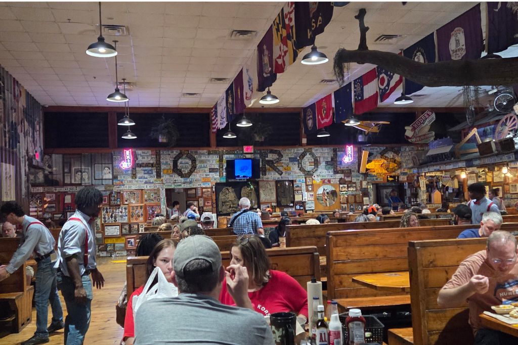 Missouri Road Trip Itinerary: Branson, The Ozarks &Amp; Beyond 23 Dining room inside lambert's cafe in missouri filled with wooden booths, vintage americana decor, and guests enjoying the famous home of throwed rolls experience.
