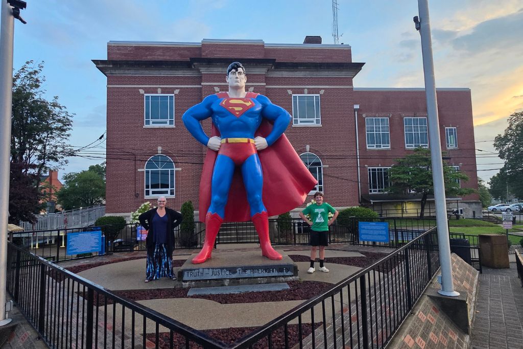 Missouri Road Trip Itinerary: Branson, The Ozarks &Amp; Beyond 24 Visitors pose beside the giant superman statue in metropolis, illinois, outside the superman museum at sunset with the super city sign in the background.