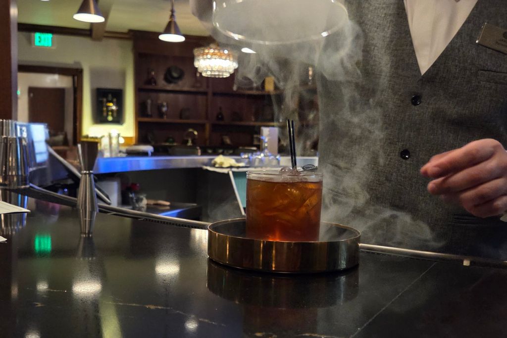 Wisconsin Dells For Adults: Beyond The Waterparks 16 Bartender at uphoffs rotunda speakeasy presents an amber cocktail as smoke curls around the glass on the bar.