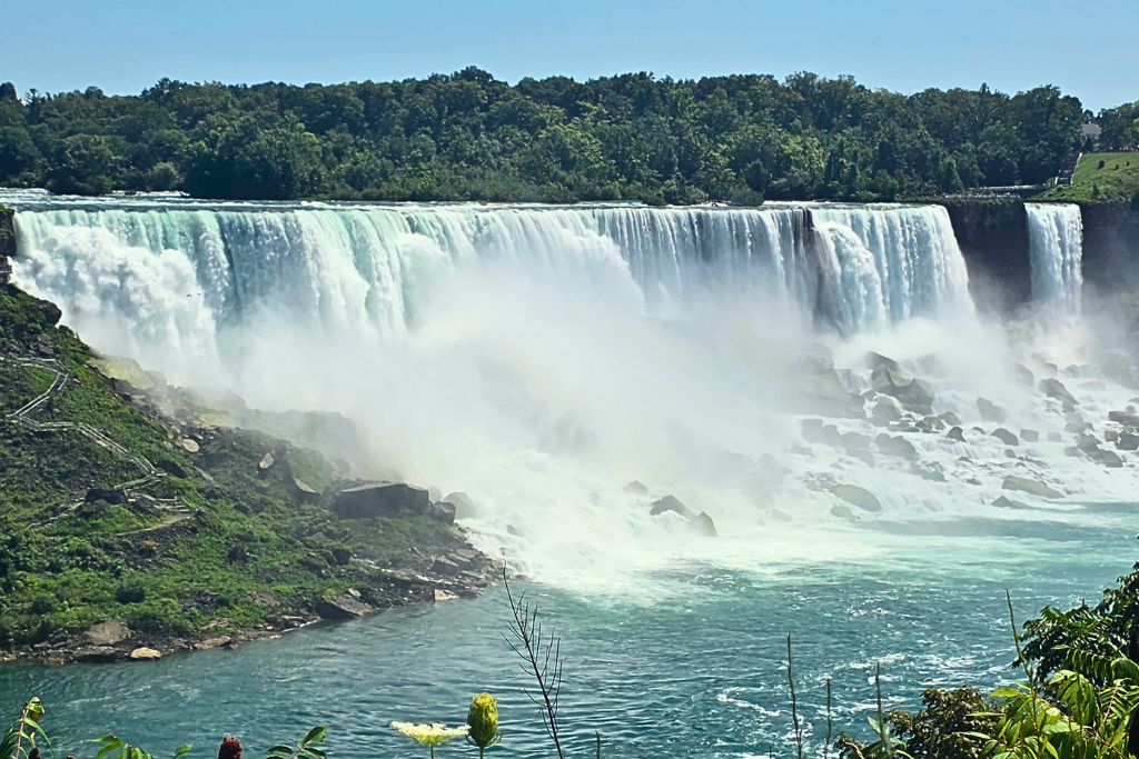 American Falls And Bridal Veil Falls From Canada American falls and the narrow bridal veil falls plunge into the niagara river with heavy mist rising from the rocks below. The canadian side offers a wide view across the river that shows the scale and power of the falls.