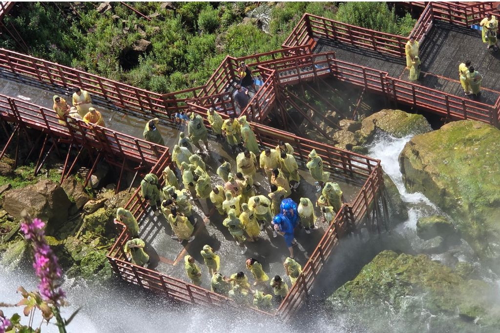 Is Niagara Falls Worth Visiting? What We Think After Several Visits 11 Cave of the winds tour viewed from luna island with visitors in yellow ponchos crowding the red walkways beside bridal veil falls. Water and mist spray across the platforms showing how close the tour brings visitors to the falls.